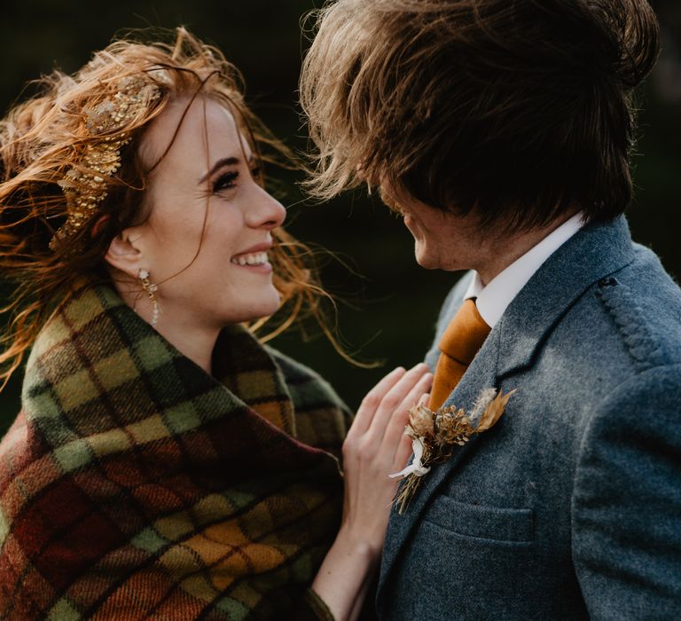 Bride leans into groom whilst wearing tartan blanket 