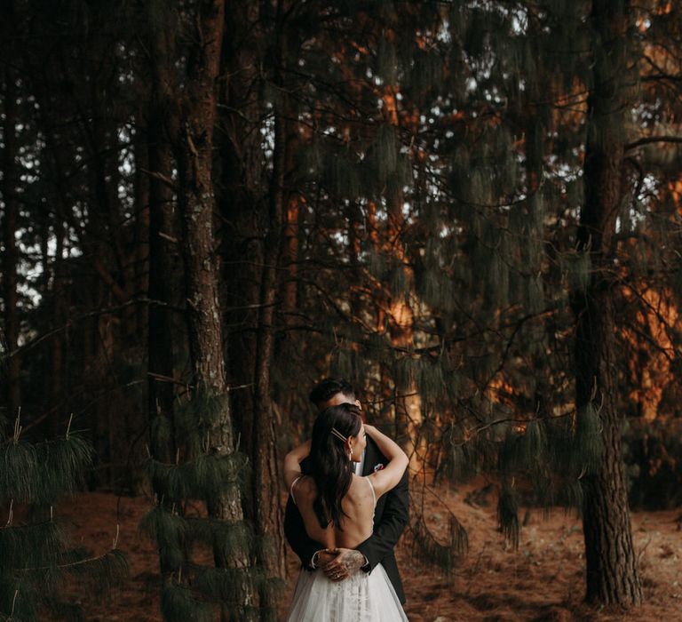 Bride and groom hug in the woods for a moody romantic wedding shoot