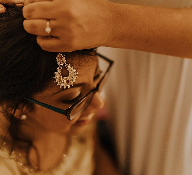 A bride gets a maang tikka put on as she gets changed for her evening party.