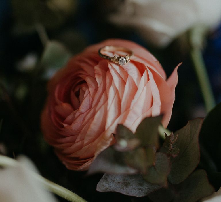 Gold wedding ring with diamond sitting on a pink rose