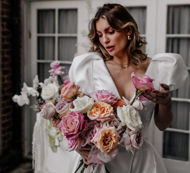 Bride in a Love In Lace bridal gown with plunging neckline holding her blush pink and white peel back rose wedding bouquet 