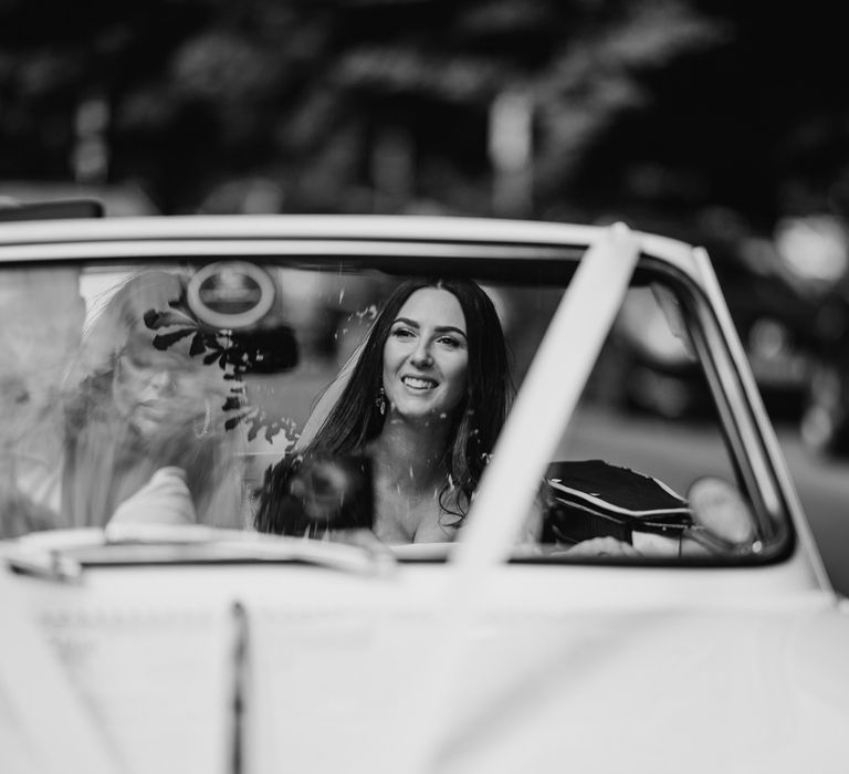 Bride smiles as she rides in vintage Triumph with guests to Harrogate wedding