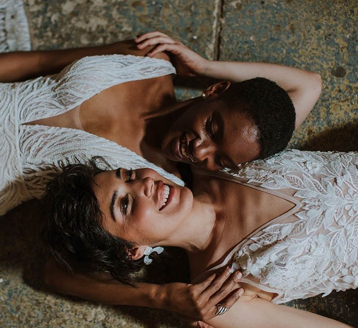 Two brides laying on the floor in an embellished wedding dress and appliqué gown with plunging necklines 