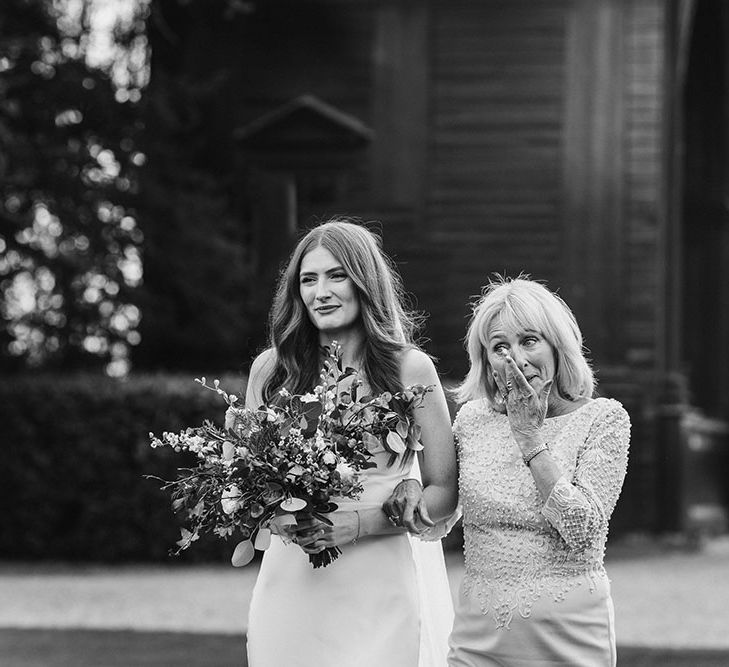 Emotional mother of the bride walking her daughter down the aisle in a satin slip wedding dress at outdoor wedding ceremony 