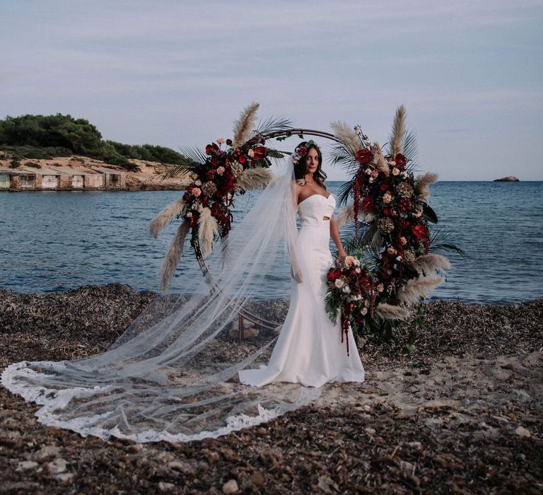 Bride wearing a Jarlo London fitted wedding dress with long flowing veil, on the beach