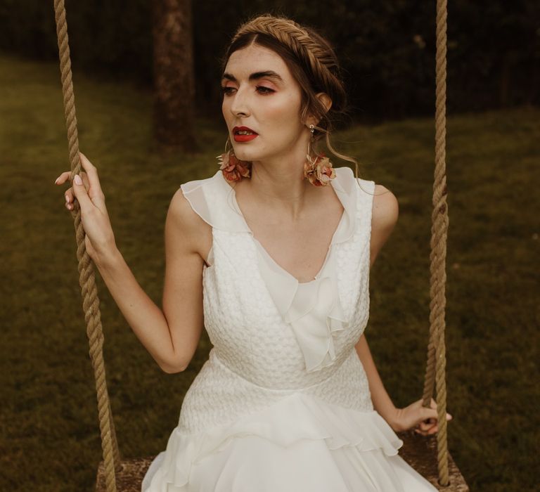 Boho bride in ruffle detail dress with braided updo and floral earrings 