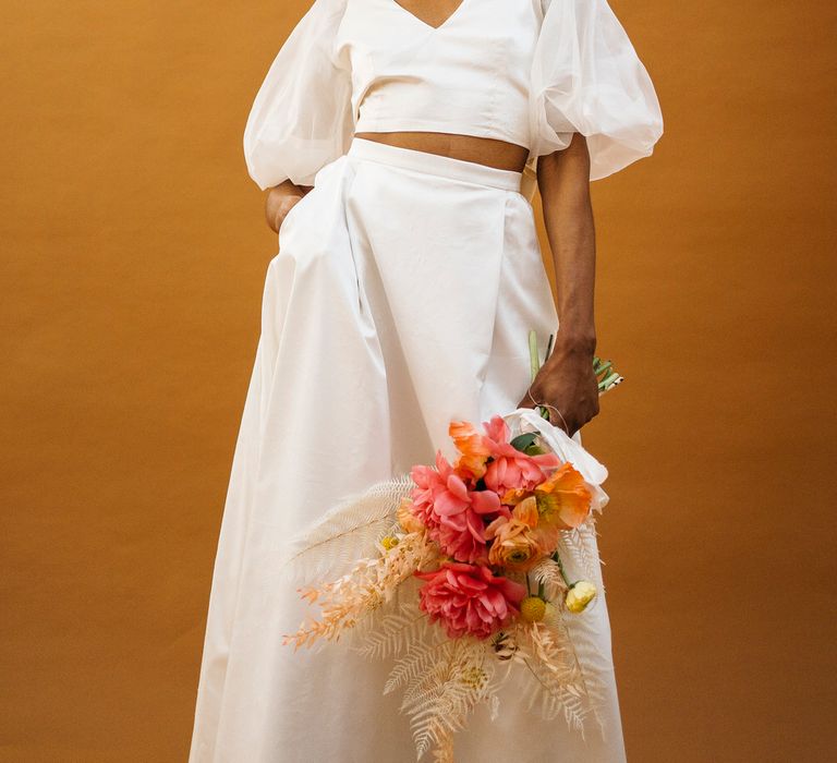 Bride wearing puff sleeve bridal separates holding a bouquet of pink flowers