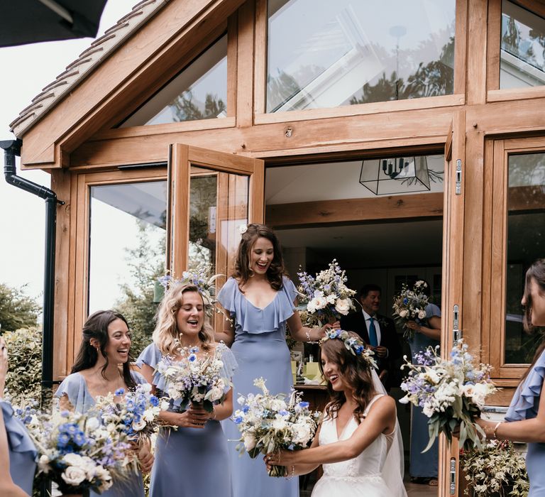 Bride leaves with her bridesmaids who wear dusty blue bridesmaids dresses holding floral bouquets