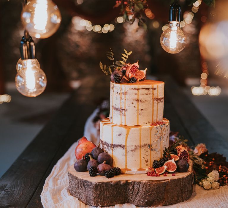 Rustic two tier white iced wedding cake for pumpkin spice wedding, with golden caramel drips and fruit decoration