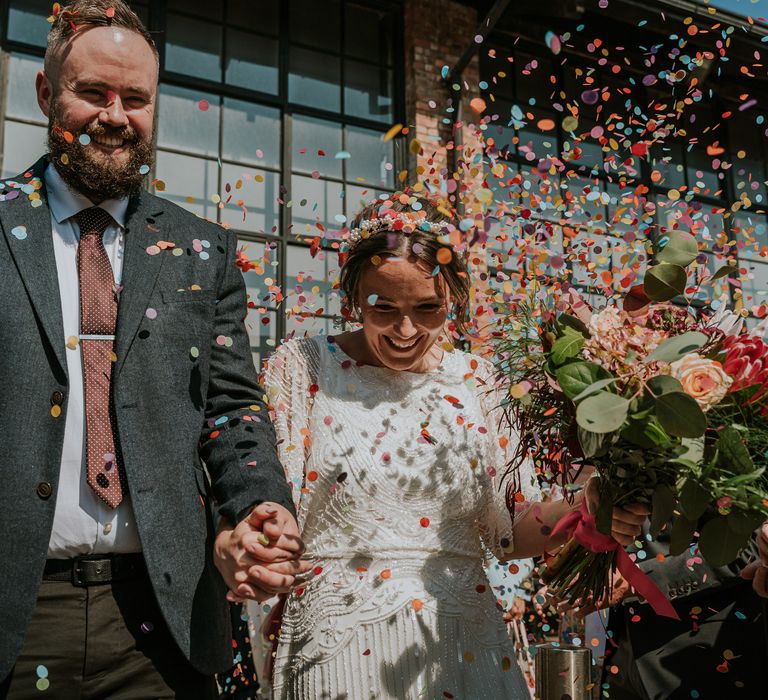 Bride & groom leave wedding ceremony as wedding guests throw brightly coloured confetti around them