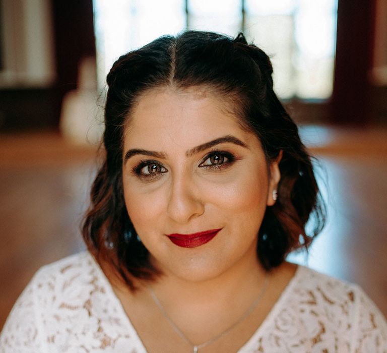 Indian bride with shoulder length hair in a lace wedding dress with bright red lipstick and smokey eye makeup 