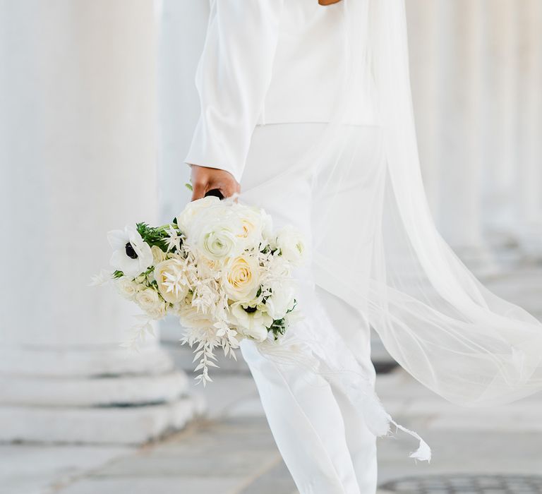 Close up shot of black and white wedding flowers. The bride wears a white suit, long veil and black shoes.