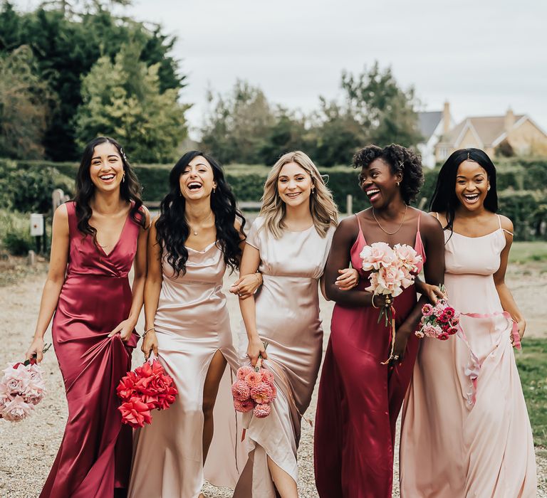 Bridesmaids in dark fuchsia pink, and pale pink Constellation Âme satin bridesmaid dresses with strapless, cap sleeve, and spaghetti strap designs 