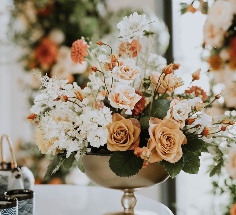 Peach and white wedding floral arrangement in a gold vessel 