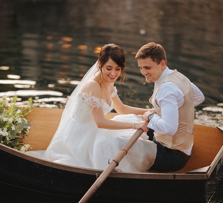 Bride & groom sit together in wooden boat on their wedding day