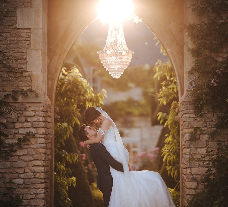 Groom lifts up his bride as the sun sets behind them on their wedding day