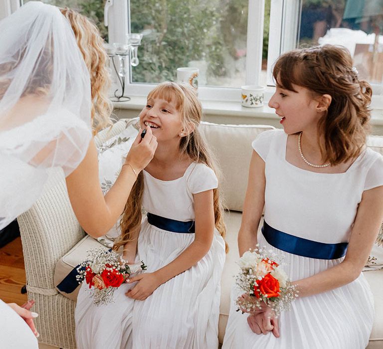 Bridesmaid wearing white dress complete with blue sash has her lipstick done on the morning of her wedding day