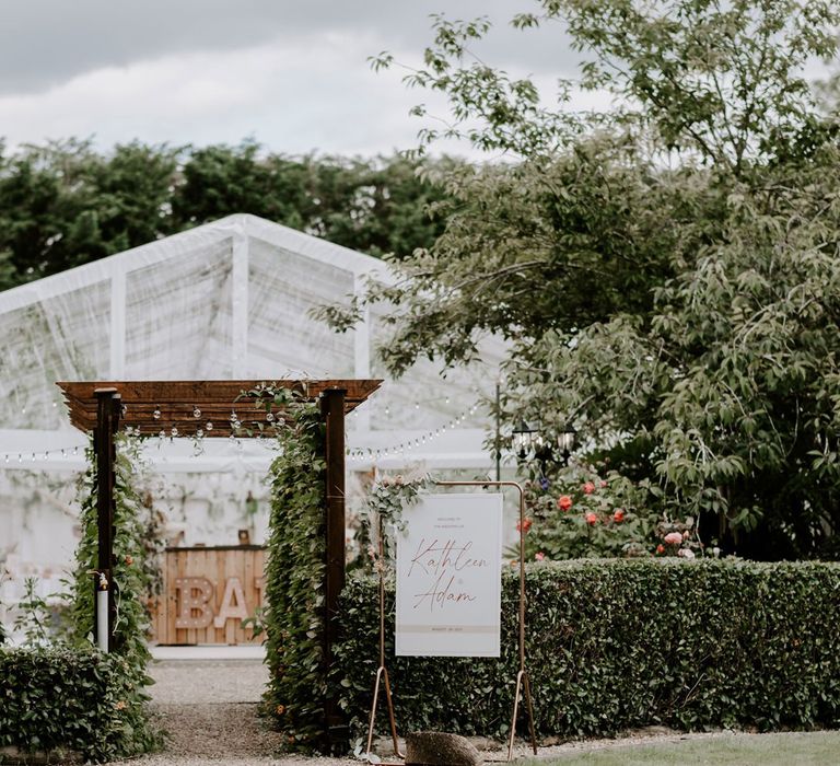 White clear sided marquee in garden with wooden bar and greenery for DIY garden wedding in Bedfordshire 