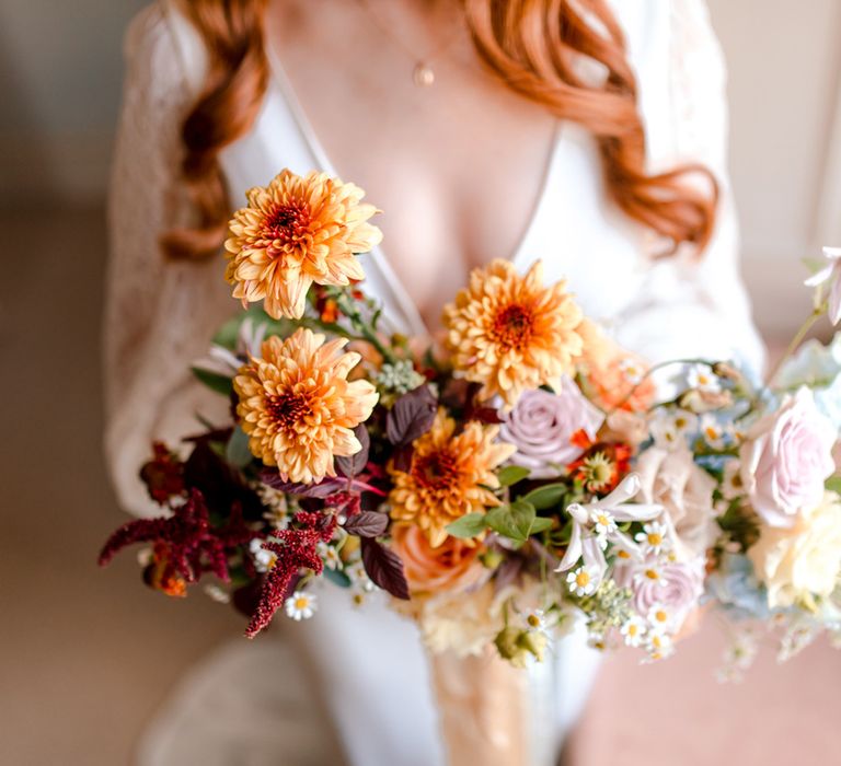 Bride in vintage wedding dress with lace sleeves holding bright multicoloured bridal bouquet with purple, orange and burgundy florals