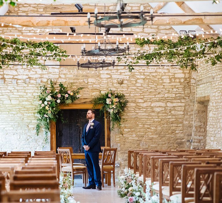 Groom in a navy suit standing at the altar of his Caswell House wedding decorated with vines and fairy lights 