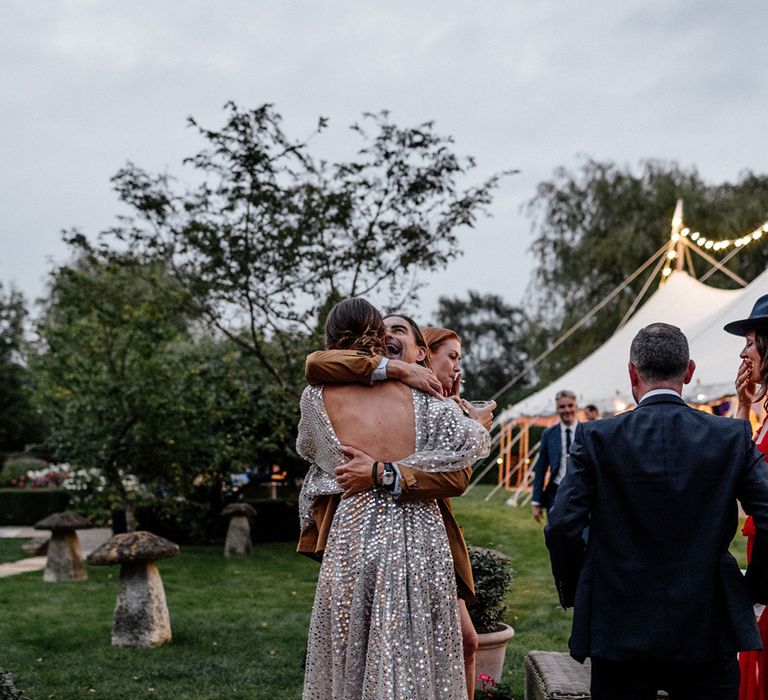 Wedding guest embracing the bride in a low back silver sequin wedding dress