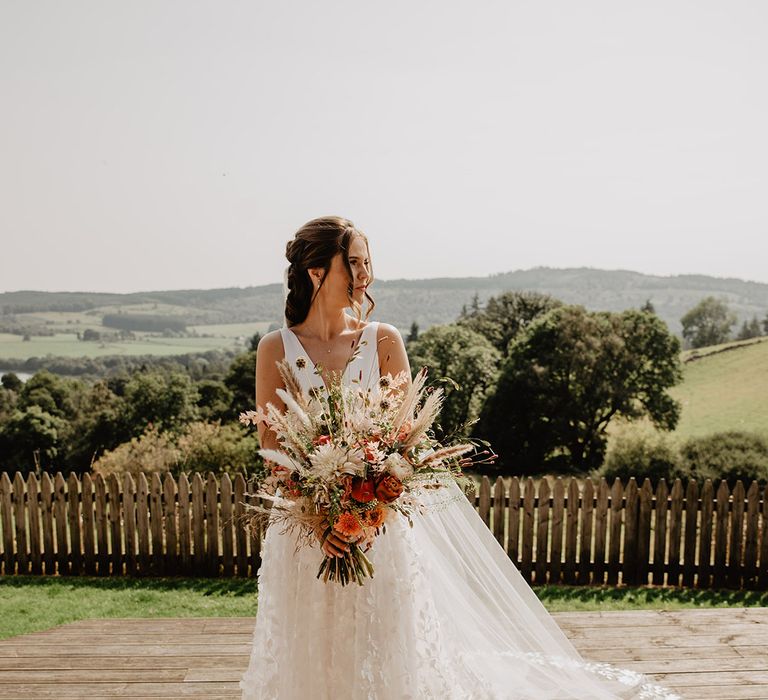 Savin London flower lace skirt wedding drss worn by bride holding autumnal wedding bouquet with Socttish hills backdrop