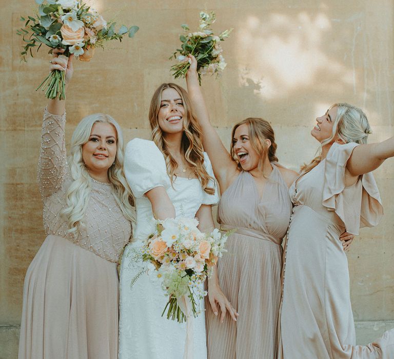 Bride in textured puff sleeve wedding dress with bridesmaids in champagne gold dresses holding pink and white flower bouquets