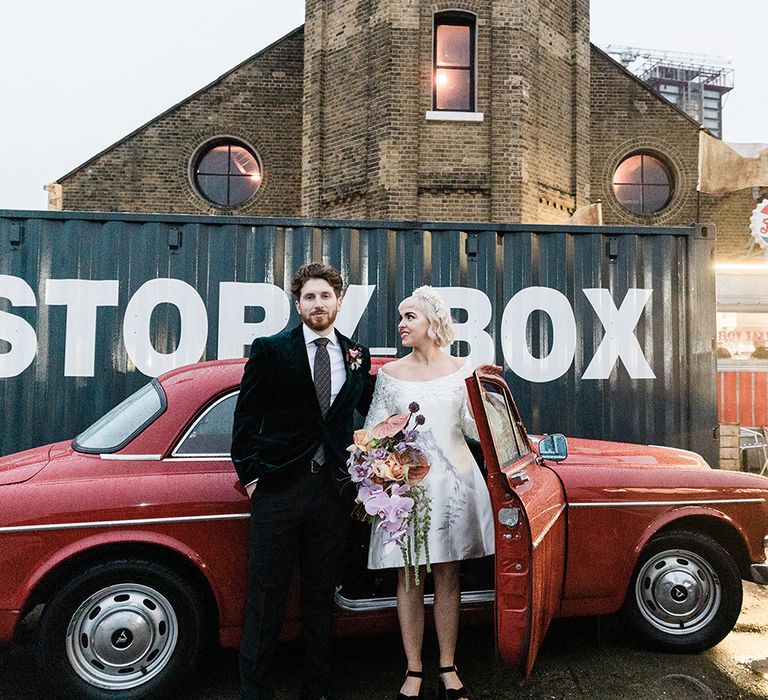 Bride and groom stand as they get out from their vintage red Volvo wedding car transport