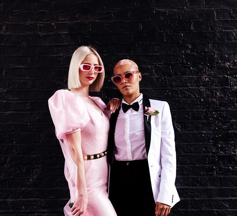 LGBTQI+ wedding inspiration with bride in a pink jumpsuit and sunglasses with her partner in a white tuxedo jacket and pink sunglasses 