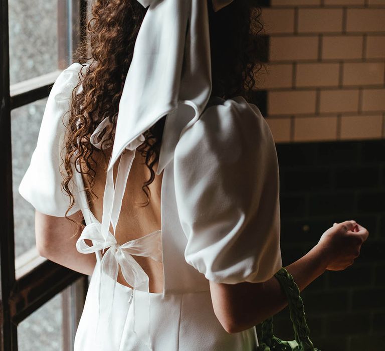 Bride in a short wedding dress with bow back detail and naturally curly hair with giant bow hair accessory 