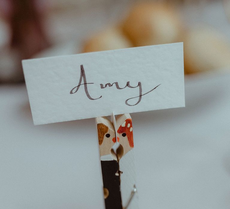 Handpainted peg with personalised picture of the bride and groom holding up place name cards 