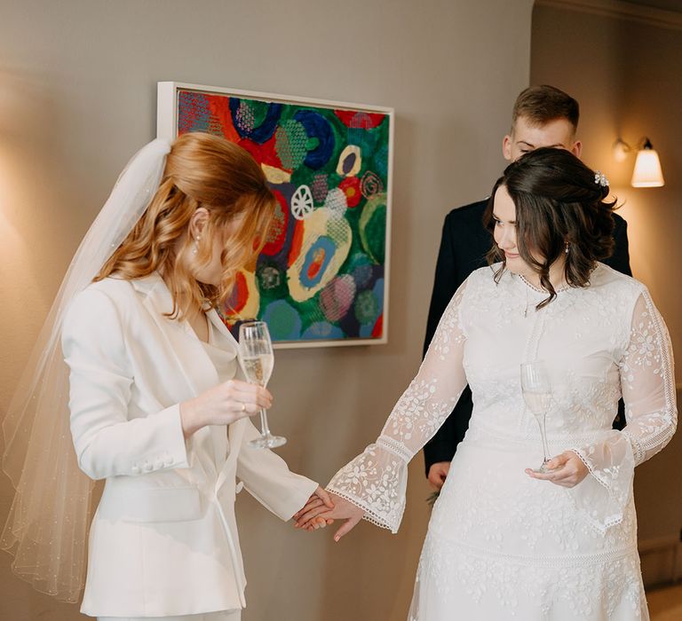 Brides hold flutes of champagne and look at one another on their wedding day