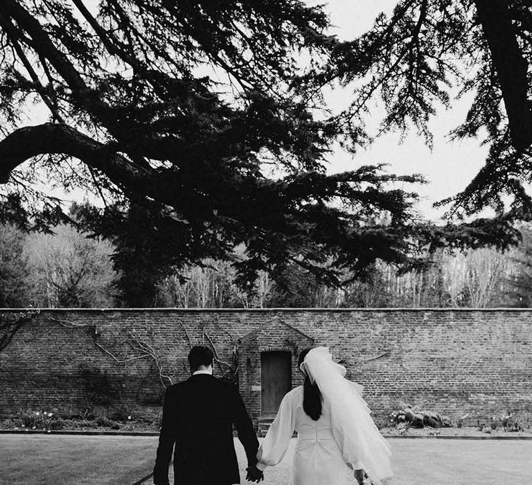 Bride in a short wedding dress wearing platform shoes, and a bow veil holding hands with her groom in a tuxedo at Garthmyl Hall 