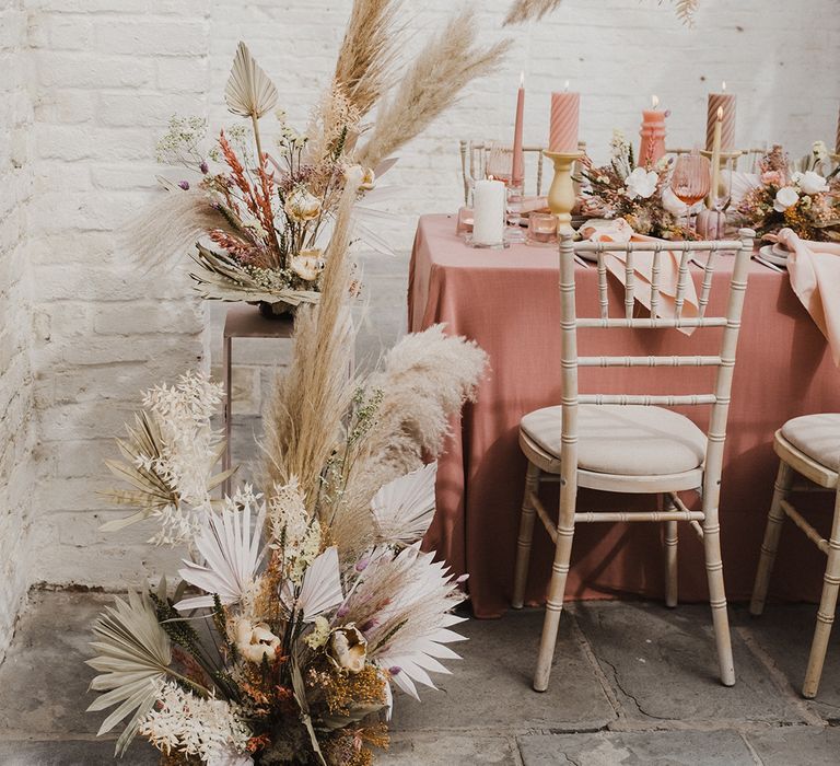 Pink table cloth, pillar candles mixed with cream candlesticks and preserved pastel flowers and dried grasses 