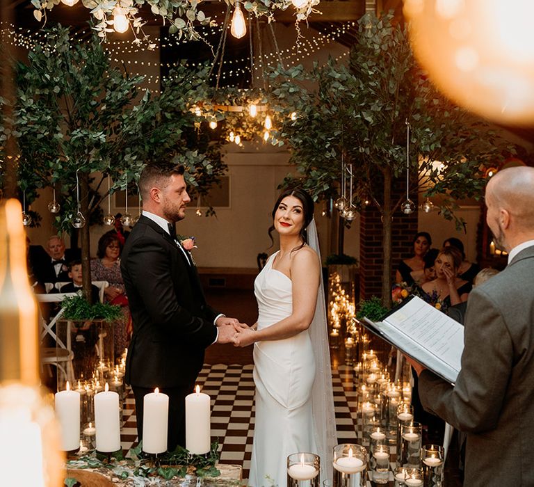 Bride in one shoulder wedding dress with red lipstick smiles holding hands with the groom during their wedding ceremony 