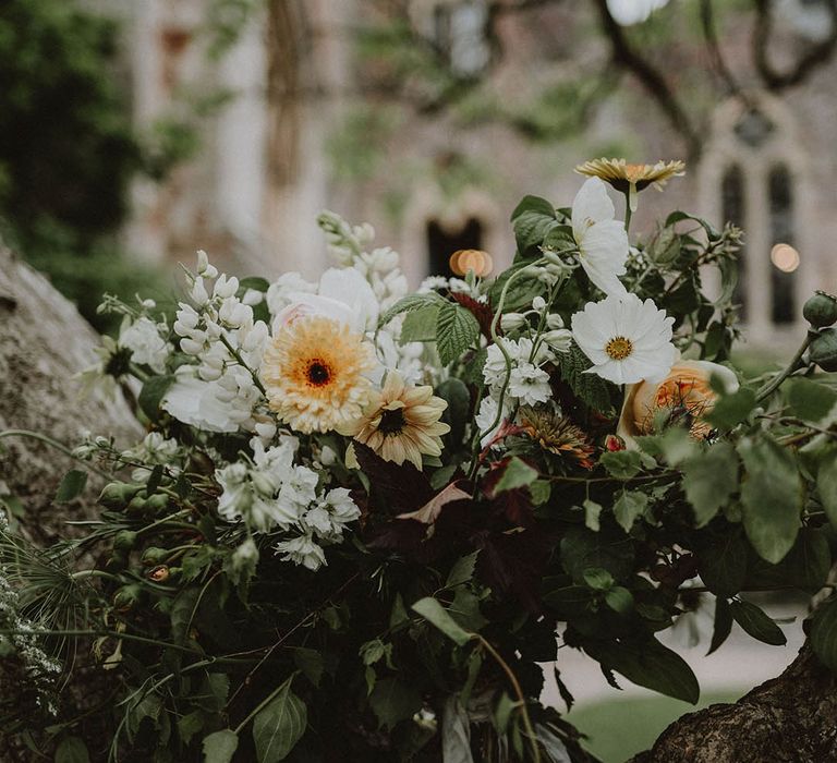 oversized green foliage, white and yellow flower wedding bouquet resting on a tree