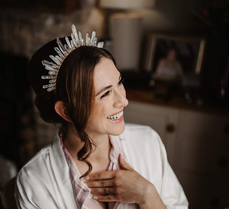 Bride in pink and white pyjamas smiles as she gets ready for the day wearing her crystal bridal crown