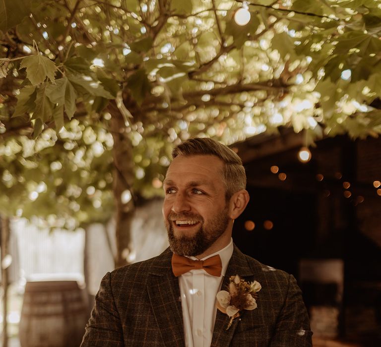 Groom in a grey checkered suit with a dried grass buttonhole 