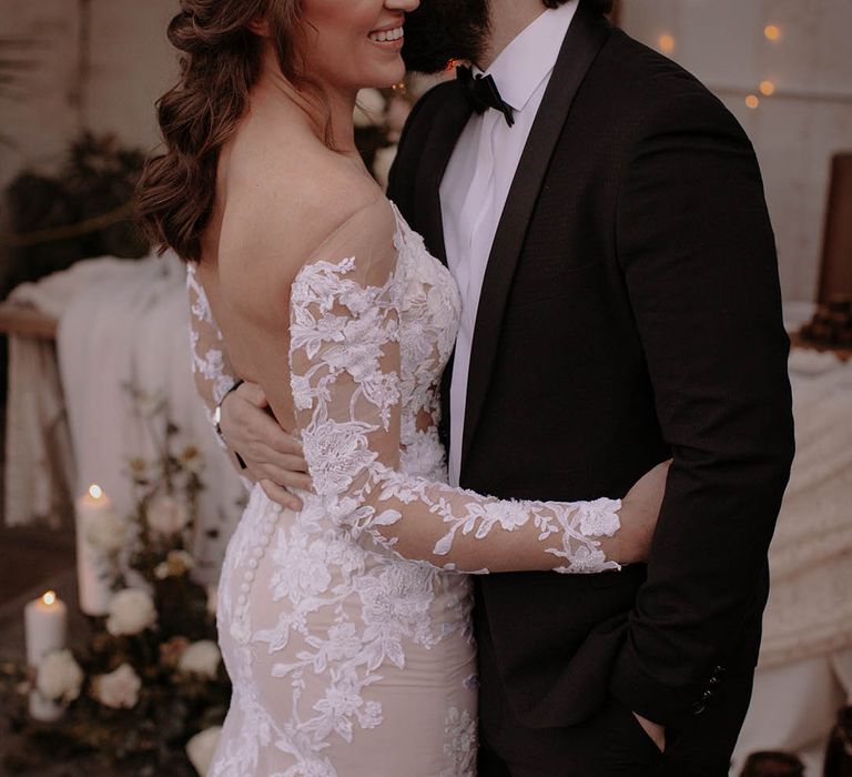 Bride in an illusion lace long sleeve low back buttoned wedding dress with the groom in black tie for their rustic winter wedding 