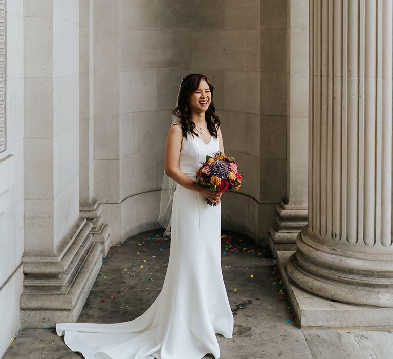 Bride holds colourful floral bouquet and wears elegant classic wedding dress 