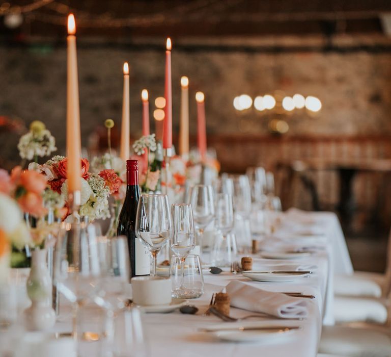 Peach and coral taper candles decorate the wedding tablescape with flowers in the same colour scheme 