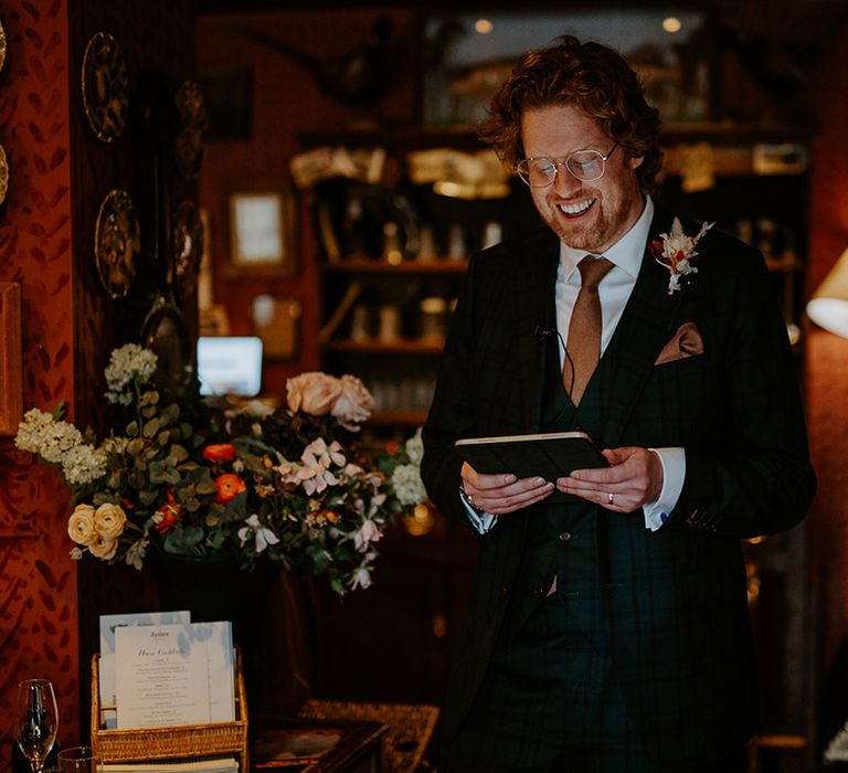 Groom in dark suit with orange tie, orange pocket square and autumnal boutonniere doing wedding reading 