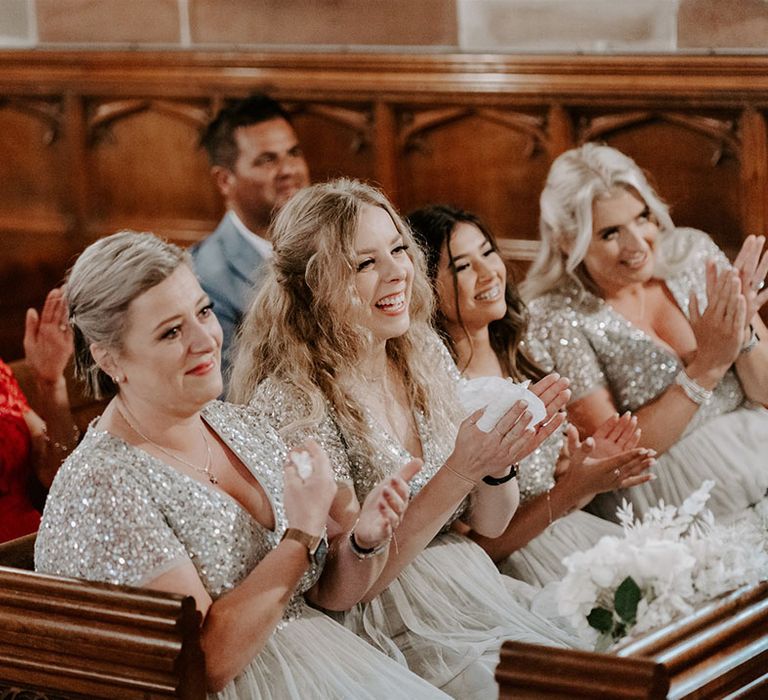 Bridesmaids sit in matching pre-loved sequin silver dresses and clap for the bride and groom 