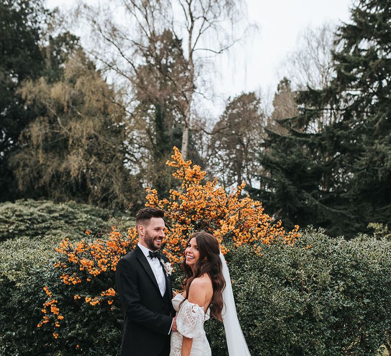 The groom smiles brightly as he embraces the bride in a boho bridal outfit on their wedding day at Hampton Manor 