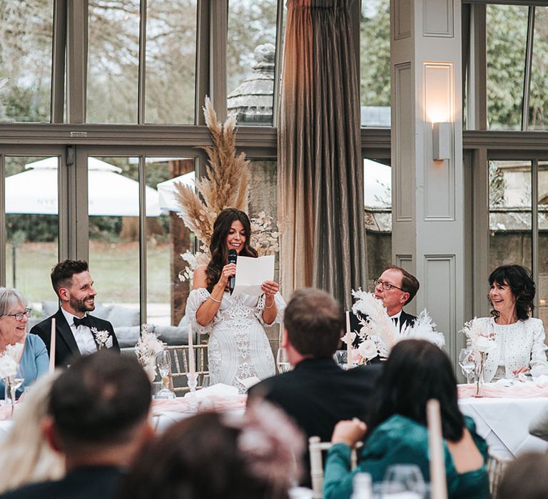 The bride stands up holding a microphone as she delivers her bridal speech 