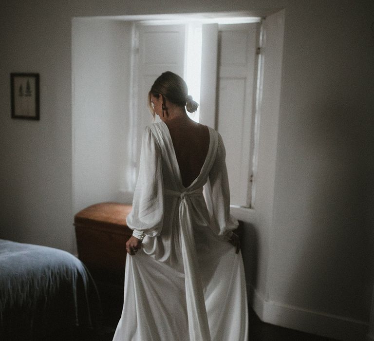 Bride wears her hair in a low bun and silk floaty wedding dress by Ailsa Munro with low back and bow 