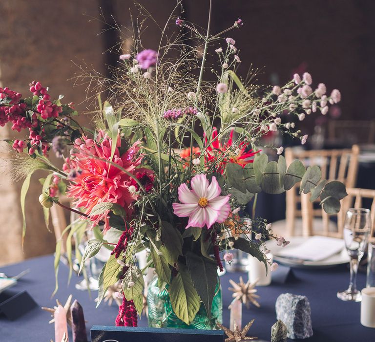 Purple, pink, orange coloured wedding flowers on a navy midnight blue table decor with gold stars and table name sign, candle favours for celestial theme