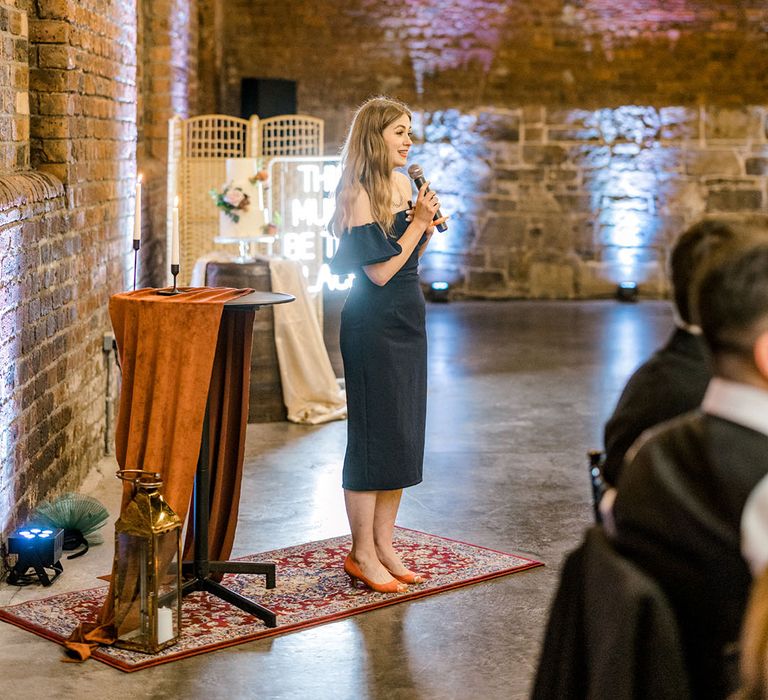 Wedding guest in off-the-shoulder black dress gives speech during wedding reception at The Engine Works