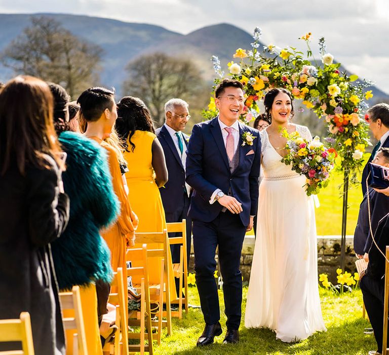 Bride holds colourful floral bouquet during outdoor wedding ceremony at Plas Dinam wedding venue 