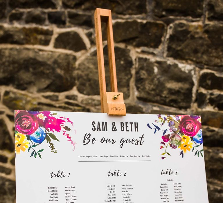 White seating chart complete with colourful floral illustrations on wooden easel 